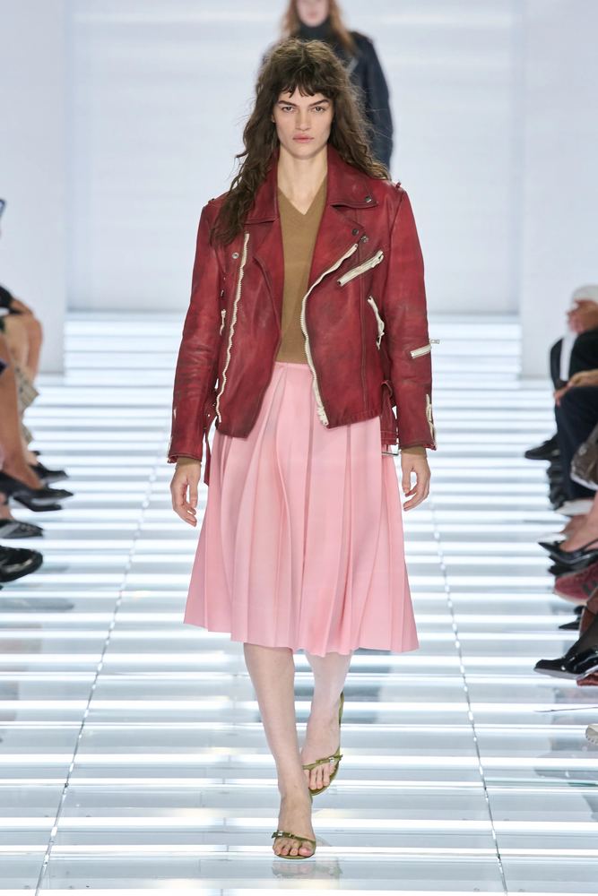Distressed oxblood leather biker jacket over a pale pink pleated midi skirt, Prada S/S 27, Milan.