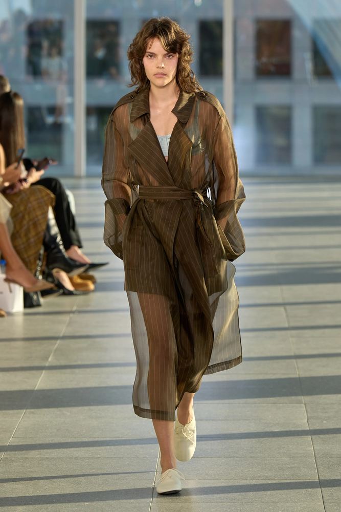 Sheer chocolate organza trench coat belted over a striped dress, Monse S/S 27, New York.